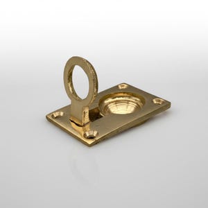 May include: A brass flush pull with a circular handle and a square base. The handle is raised, and the base has four screw holes. The hardware has a shiny, golden finish.