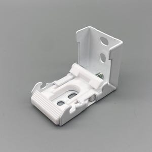 Może przedstawiać: Biały metalowy wspornik do żaluzji o konstrukcji kątowej. Posiada szereg szczelin i otworów do montażu, a także plastikowy element i śrubę. Wspornik jest przeznaczony do mocowania żaluzji.