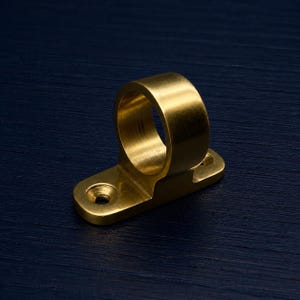 May include: A brass-coloured ring-shaped fitting with a rectangular base. The base has two holes for mounting. The fitting is made of a shiny, metallic material.