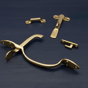 May include: A selection of brass hardware components, including a handle, a latch, and two smaller brackets. The items are displayed on a dark blue surface, highlighting their polished, golden finish. These are likely for cabinetry or furniture.