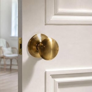 May include: A round, brushed brass door knob mounted on a white panelled door. The knob features a spherical handle attached to a circular base plate, with a rectangular brass latch plate visible on the edge of the door frame.