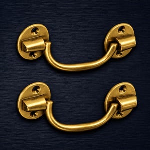 Peut inclure: Deux poignées de tiroir en laiton assorties présentant un design incurvé de type tombant. Chaque poignée est fixée par deux plaques de montage circulaires, chacune comportant deux trous de vis, offrant un élément de quincaillerie fonctionnel.