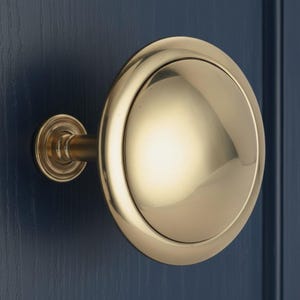 May include: A polished brass door knob with a large, circular design. The knob is mounted on a dark blue door, showcasing its reflective surface and classic style. The knob's design includes a small, decorative stem.