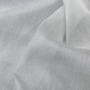 May include: Close-up of a white, loosely woven fabric with a textured, grid-like pattern. The material is draped, creating soft folds and shadows. The fabric appears lightweight and semi-transparent.