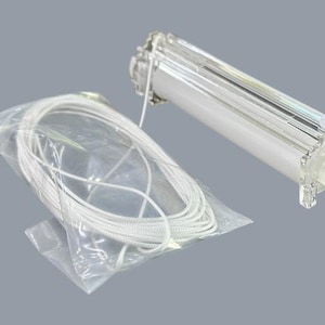 May include: A clear plastic window blind mechanism with a white cord in a plastic bag. The mechanism is rectangular with a white roller and clear plastic supports. The background is a solid grey.