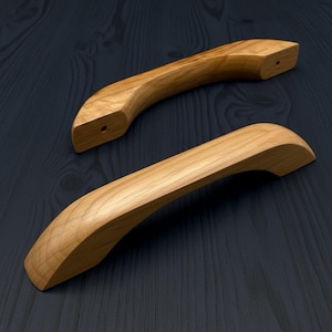 Può includere: Due maniglie per armadietti in legno curvato con una finitura a venature naturali color marrone chiaro. Ogni maniglia presenta un design liscio e arcuato con un singolo foro di montaggio preforato visibile sull'estremità della maniglia superiore.
