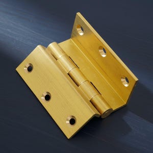 Puede incluir: Una bisagra en ángulo recto de color latón con múltiples orificios para tornillos. La bisagra está hecha de metal y tiene una serie de cilindros entrelazados en el punto de pivote. La bisagra está diseñada para su uso en puertas u otros muebles.