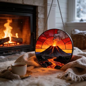 May include: A round stained glass panel depicting a volcano erupting, with a fiery red and orange sky. The panel is suspended by a chain. A cup of tea sits on a saucer in front of a fireplace.