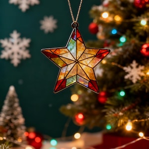 May include: A stained glass star-shaped ornament with a gold chain. The star features a mosaic of warm colors, including red, orange, yellow, and green. The ornament is hanging in front of a Christmas tree with colorful lights and ornaments.