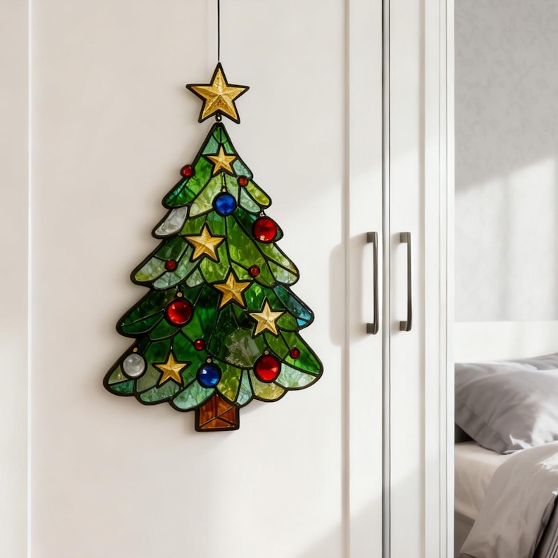 K&ouml;nnte beinhalten: Ein Weihnachtsbaumschmuck aus Glasmalerei. Der Baum ist gr&uuml;n mit goldenen Sternen, roten und blauen Kugeln und einem goldenen Stern an der Spitze. Der Baum h&auml;ngt vor einem wei&szlig;en Hintergrund.