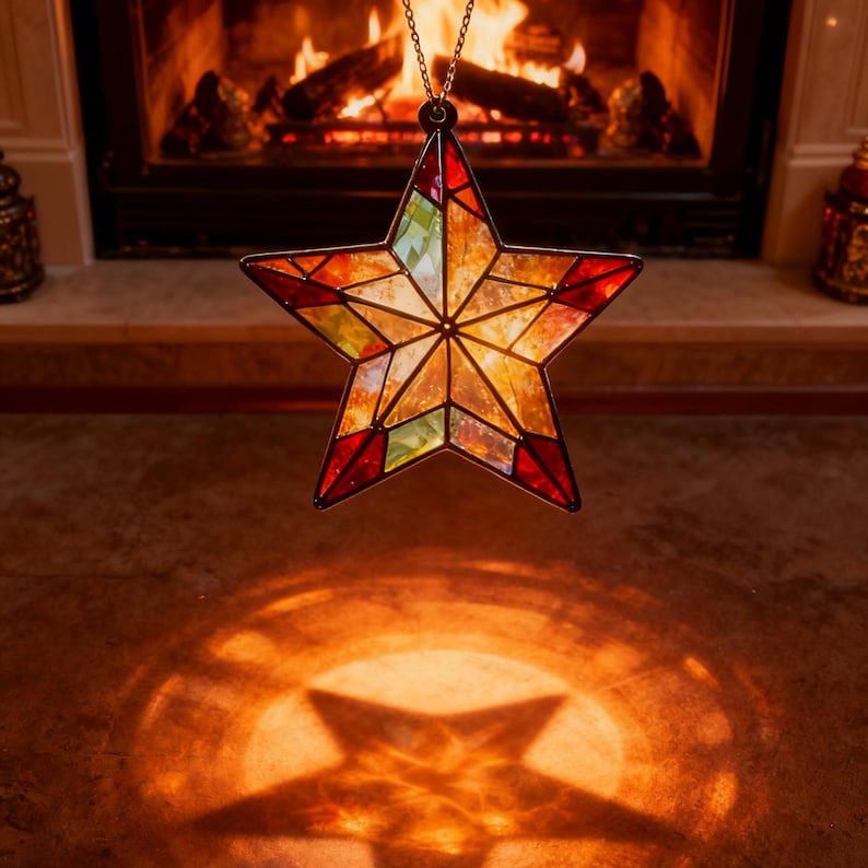 May include: A stained glass star-shaped ornament with red, green, and yellow panels hangs from a gold chain. The star's shadow is cast on the floor below. A fireplace with a burning fire is in the background.