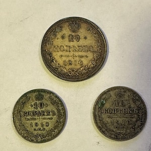 May include: Three antique silver coins. The top coin is a 20 kopek coin from 1910. The two bottom coins are 10 kopek coins from 1910. All coins have Cyrillic text and a crown design.