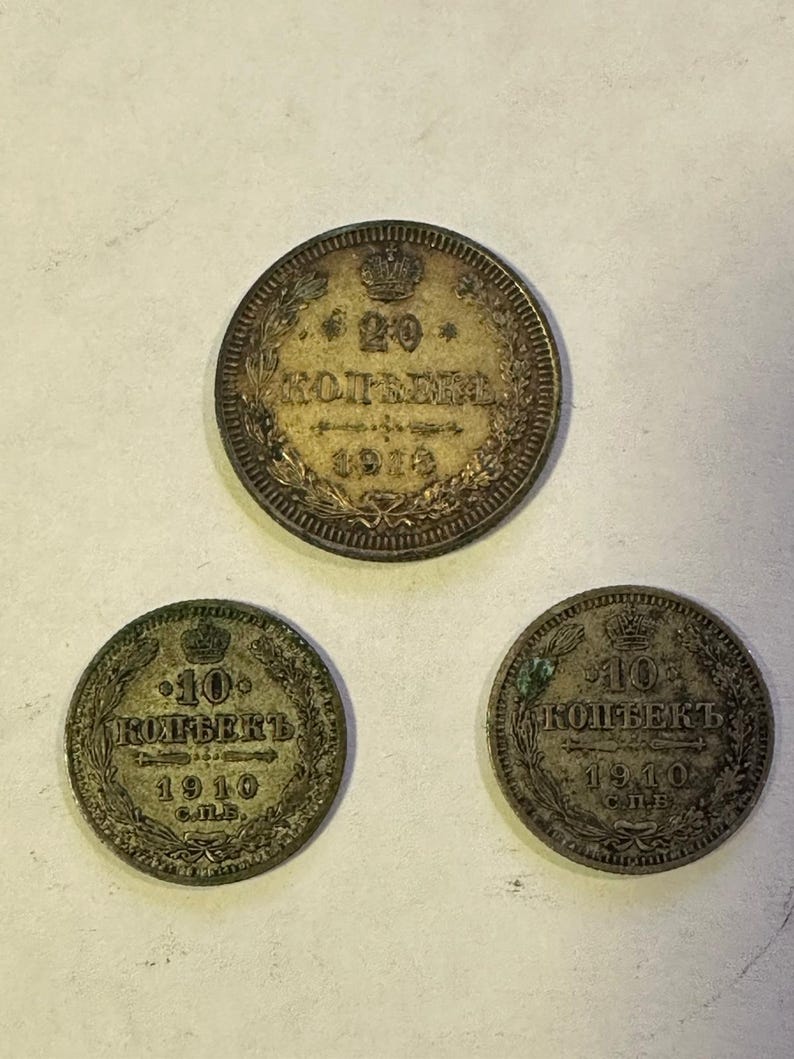 May include: Three antique silver coins. The top coin is a 20 kopek coin from 1910. The two bottom coins are 10 kopek coins from 1910. All coins have Cyrillic text and a crown design.