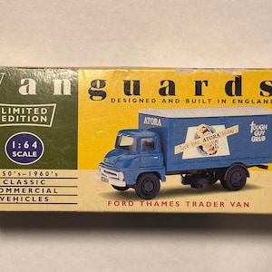 以下が含まれることがあります： 1950～1960年代の青いフォード・テムズ・トレーダー・バンの1:64スケールモデル。箱には「Vanguards」のロゴ、「Limited Edition」の文字、「Tough Guy Grub」のブランドが表示されています。