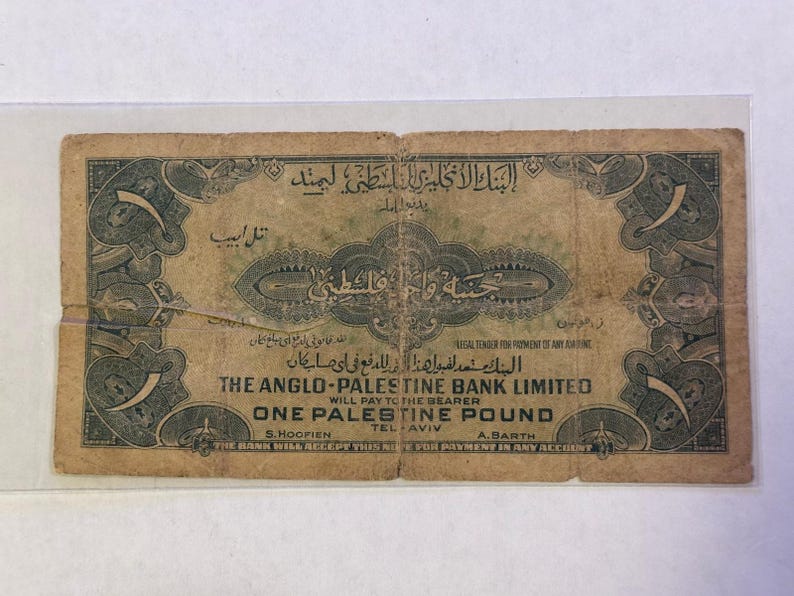 May include: An antique one Palestine pound banknote. The note is primarily tan with dark green ornate borders and text in English and Arabic. The text includes "The Anglo-Palestine Bank Limited" and "One Palestine Pound".