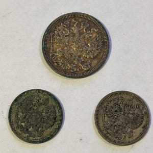 May include: Three antique silver coins with detailed embossed designs. The coins feature a double-headed eagle emblem, likely of historical significance. The coins are circular and show signs of age and wear.