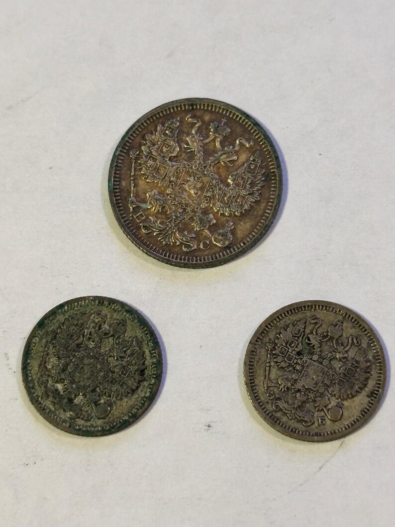May include: Three antique silver coins with detailed embossed designs. The coins feature a double-headed eagle emblem, likely of historical significance. The coins are circular and show signs of age and wear.