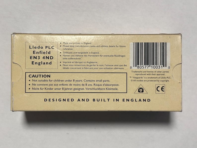 以下が含まれることがあります： 「Lledo PLC Enfield EN3 4ND England」と「Designed and Built in England」などのテキストが記載された、ベージュ色の段ボール箱。 バーコードと小さな部品に関する警告があります。 この箱は玩具用です。