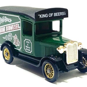 K&ouml;nnte beinhalten: Ein gr&uuml;ner und schwarzer Vintage-Spielzeug-LKW mit goldfarbenen R&auml;dern und Akzenten. Der LKW tr&auml;gt den Text "Anheuser-Busch Genuine Budweiser" an der Seite und "KING OF BEERS" auf dem Dach.