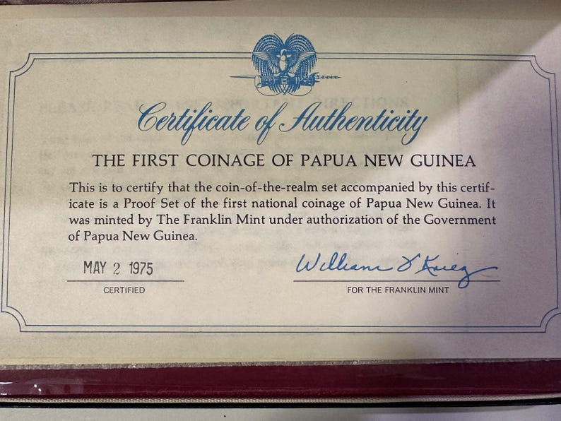 Pode incluir: Certificado de autenticidade da primeira cunhagem da Papua Nova Guin&eacute;, datado de 2 de maio de 1975. O documento certifica um Proof Set cunhado pela The Franklin Mint. Apresenta um emblema azul e uma assinatura.