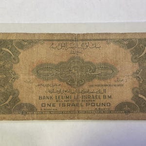 Puede incluir: Un antiguo billete de una libra israel&iacute;, con intrincadas escrituras &aacute;rabes y bordes decorativos. El billete est&aacute; impreso en tonos marrones y beige, con texto que indica que es de curso legal. El Banco Leumi Le-Israel B.M. tambi&eacute;n est&aacute; impreso.