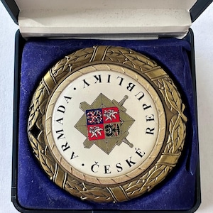 Op de afbeelding: Ronde, bronskleurige medaille met een wit midden, met een wapen en Tsjechische tekst. De medaille is omgeven door een laurierkrans en wordt gepresenteerd in een zwarte doos met een blauwe fluwelen voering.