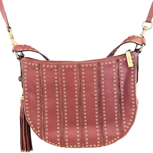 May include: A reddish-brown leather crossbody bag with gold-colored rivets and hardware. The bag has a curved shape, a long adjustable strap, and a tassel. The bag is a stylish accessory.