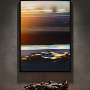 Peut inclure: Impression encadrée de deux voitures de Formule 1 en course sur une piste, avec un arrière-plan flou du ciel. Une maquette de voiture de course est posée sur une étagère en dessous. Les voitures sont noires et orange.
