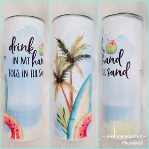 May include: A white tumbler with a blue and green watercolor design of palm trees, a surfboard, and a watermelon. The text "drink in my hand toes in the sand" is printed on the tumbler.