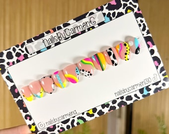 Puede incluir: Un conjunto de uñas postizas con una variedad de diseños coloridos. Cada uña presenta un patrón diferente, incluyendo rayas, lunares y formas abstractas en tonos de rosa, amarillo, verde y negro. Las uñas se muestran en una tarjeta blanca con el texto "NailsByCarmen".