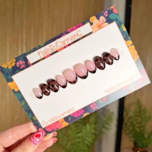 May include: A set of oval-shaped press-on nails. Some nails have a light pink base with a dark brown tortoiseshell design, while others have a light pink base with a dark brown tip. The nails are displayed on a floral patterned card with the text "nailsbyCarmenG".