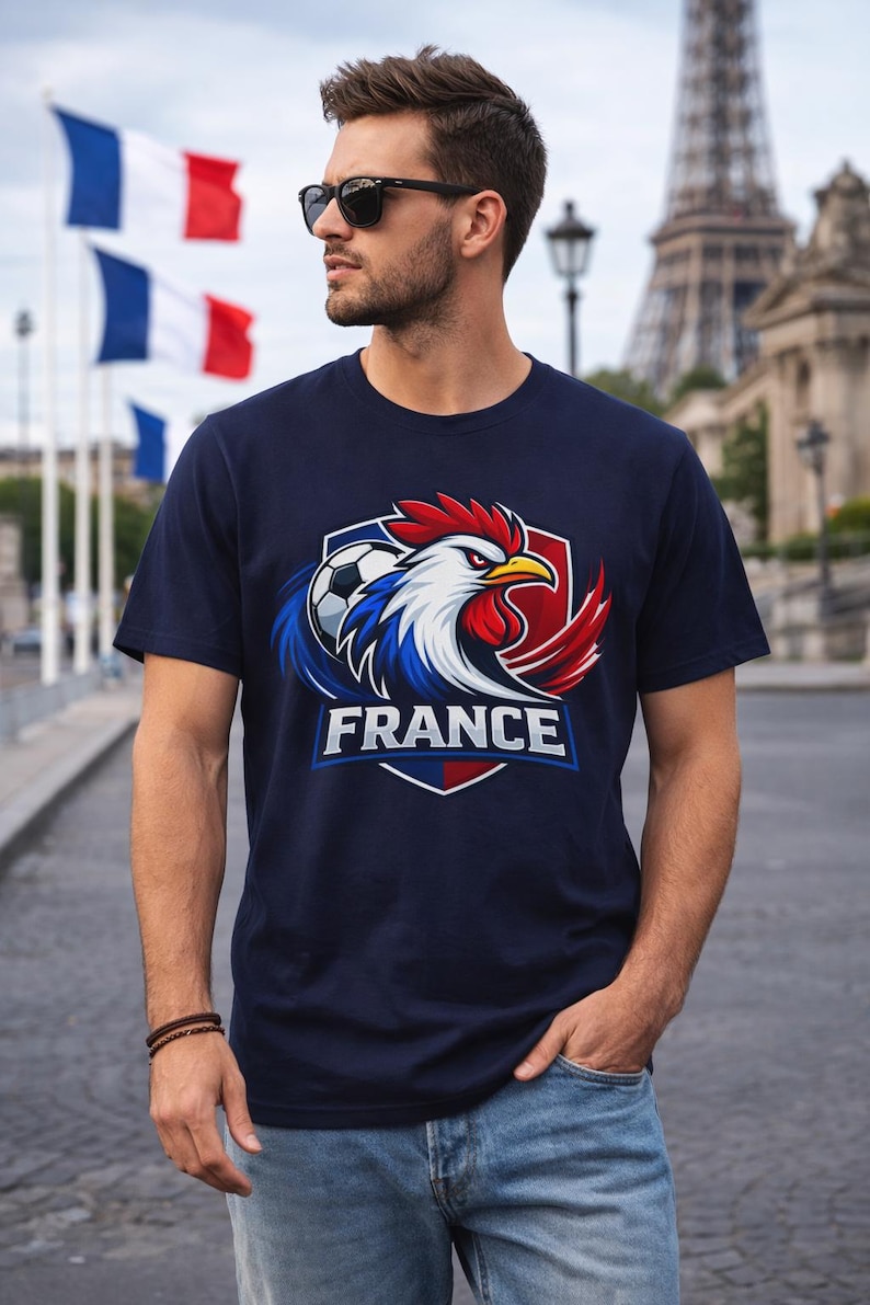 May include: Navy blue t-shirt featuring a graphic of a rooster, soccer ball, and the word "FRANCE" in white. The rooster has red, white, and blue feathers. The Eiffel Tower and French flags are in the background.