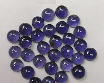 May include: A collection of round, polished, purple glass beads. The beads have a glossy finish and varying shades of purple, with some appearing darker than others. The arrangement is scattered, creating a visually appealing display of the translucent spheres.