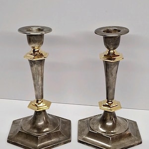 May include: A pair of silver candlesticks with gold detailing. The candlesticks have a hexagonal base and a tapered design. Gold accents are at the base of the candle holder and the top of the stem.
