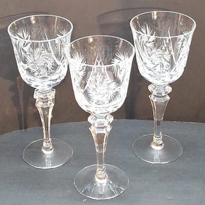 Peut inclure: Trois verres à vin en cristal clair avec des motifs floraux gravés. Chaque verre présente une base ronde, une tige facettée et un sommet en forme de bol. Les verres sont disposés sur une surface sombre, mettant en valeur leur élégance.