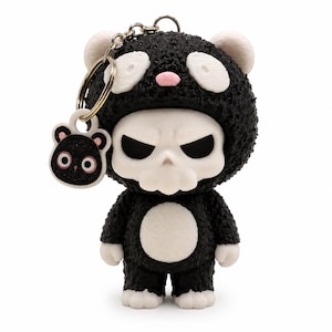 May include: A keyring featuring a small figurine of a character wearing a black textured bear costume with white accents on the ears, face, and belly. The character has a white skull-like face and a small dangling charm shaped like a bear head.