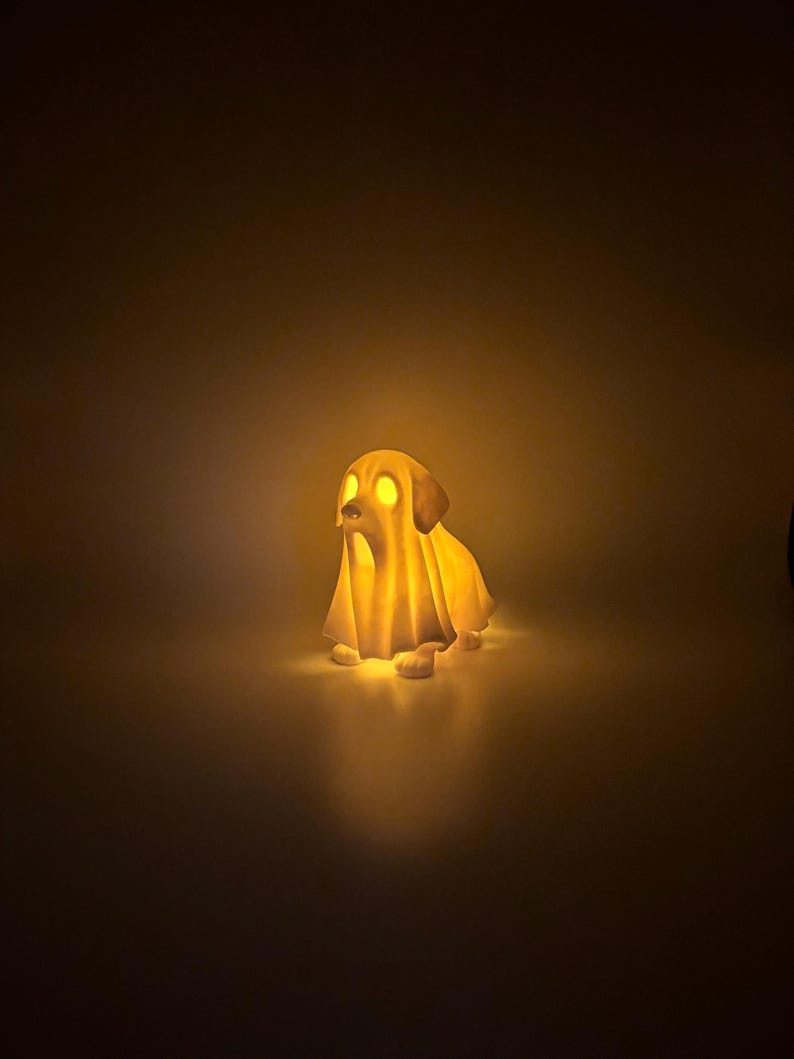 May include: A glowing, dog-shaped Halloween decoration. The figure is covered in a white sheet, with glowing yellow eyes and a warm, inviting light emanating from within. The dog is in a sitting position.