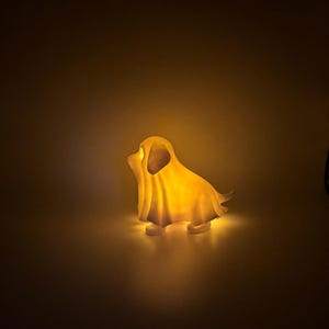 May include: A glowing, dog-shaped night light. The light is a warm yellow color, casting a soft glow. The dog is in a sitting position, with its ears and tail visible. The light is on a plain background.