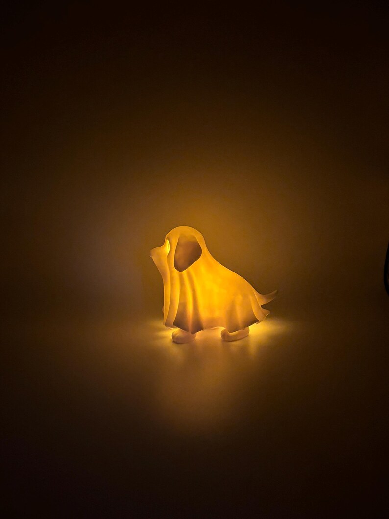 May include: A glowing, dog-shaped night light. The light is a warm yellow color, casting a soft glow. The dog is in a sitting position, with its ears and tail visible. The light is on a plain background.