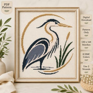 May include: A cross-stitch pattern featuring a blue and white heron standing in water with green reeds, framed by a gold circular border. The text reads PDF Pattern, Digital Download, Pattern Only, 130 x 144 Stitches, 8 DMC Colors, Use 2 Strands.