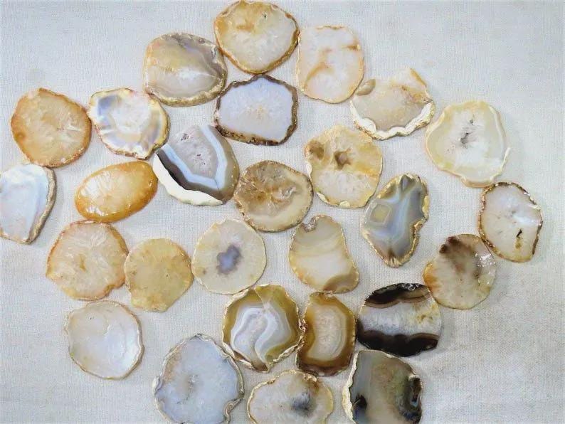 May include: A collection of polished agate slices in various shapes and sizes. The slices display a range of colors, including white, beige, brown, and gray, with natural patterns and textures. These decorative stones are ideal for crafting or display.