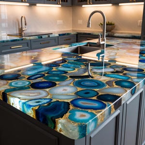 May include: A kitchen countertop with a unique design. The surface is made of blue and white agate slices with gold accents. The countertop is installed on gray cabinets with gold hardware. A stainless steel faucet is visible.