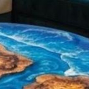 May include: Close-up of a round table with a blue and brown epoxy resin design. The blue resin simulates ocean water, and the brown resin represents landmasses. The table's edge is visible, showing the depth of the resin.
