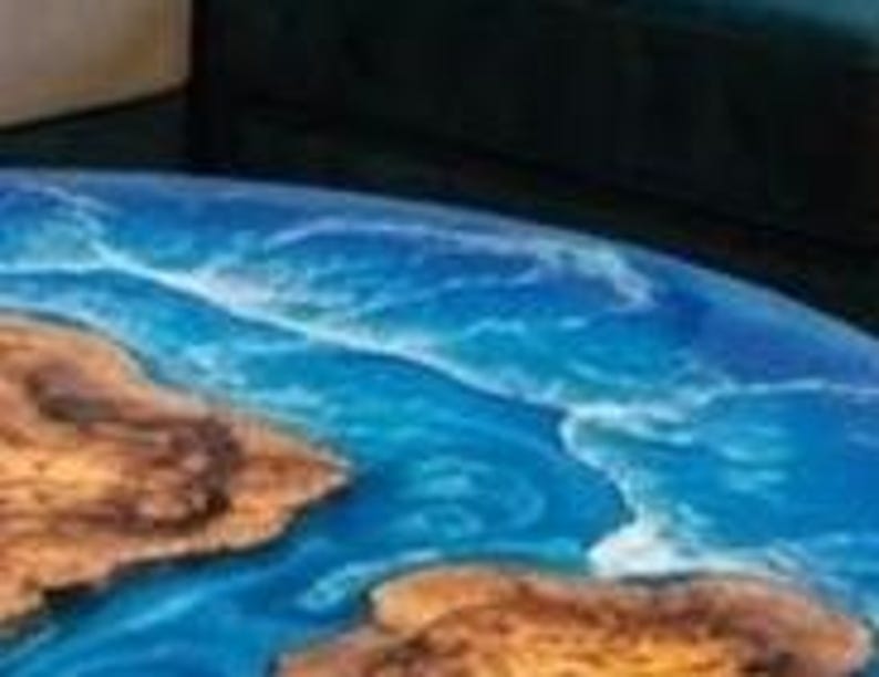 May include: Close-up of a round table with a blue and brown epoxy resin design. The blue resin simulates ocean water, and the brown resin represents landmasses. The table's edge is visible, showing the depth of the resin.