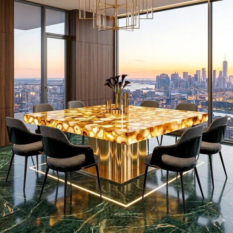 May include: A luxurious dining room set featuring a large square table with a golden, agate-like surface. The table is surrounded by six black chairs with gray cushions. The room has a city skyline view and a modern chandelier.
