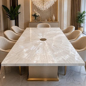 Pode incluir: Uma grande mesa de jantar retangular com um tampo branco com padrão de raios de sol e uma base bege. Oito poltronas creme com pernas douradas circundam a mesa. A sala possui um lustre, plantas e piso de mármore.