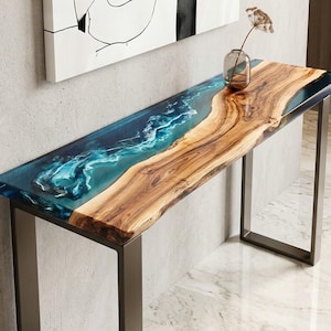 May include: A rectangular console table featuring a natural live-edge wood slab combined with a translucent blue resin inlay that mimics flowing water. The table is supported by a sturdy, dark metal frame with two rectangular legs.