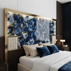 May include: A rectangular headboard featuring a large panel of blue and white agate stone slices framed in gold metal. The headboard includes integrated LED lighting and two square, quilted cream-colored side panels, positioned above a bed with pillows.