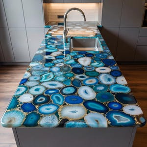 Puede incluir: Isla de cocina con encimera de rodajas de ágata azul y blanca. La ágata está engastada en resina dorada, creando un patrón de mosaico. Se ven un fregadero y un grifo de acero inoxidable.