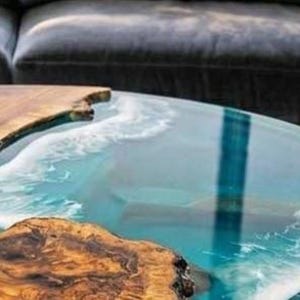 May include: A unique coffee table with a live edge wood design and a clear epoxy resin top, creating a coastal ocean wave effect. The wood has a natural, warm brown color, contrasting with the blue and white resin. The table is a decorative furniture piece.